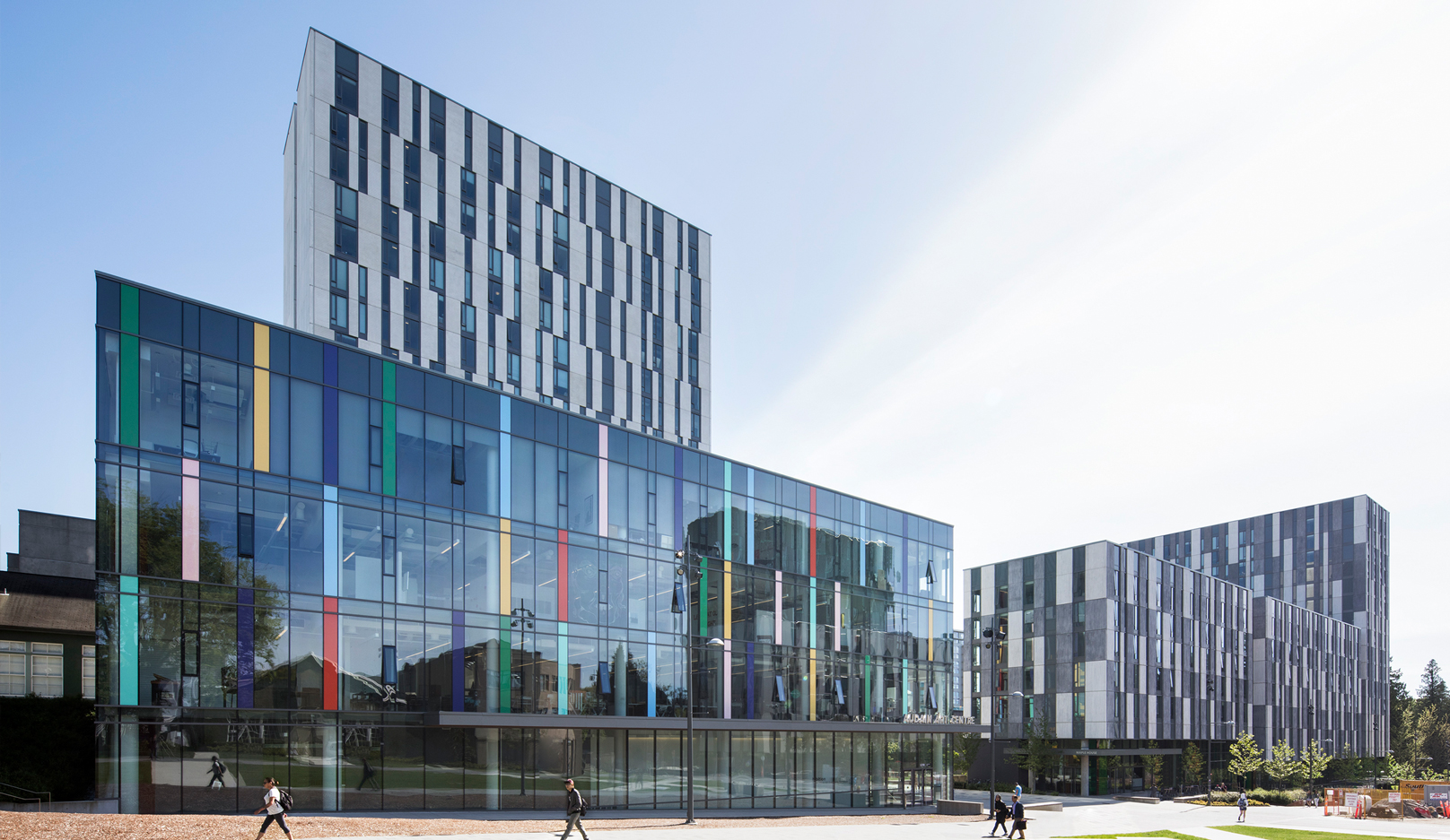 Street view of a glass building with vertical coloured rectangles scattered along the windows.
