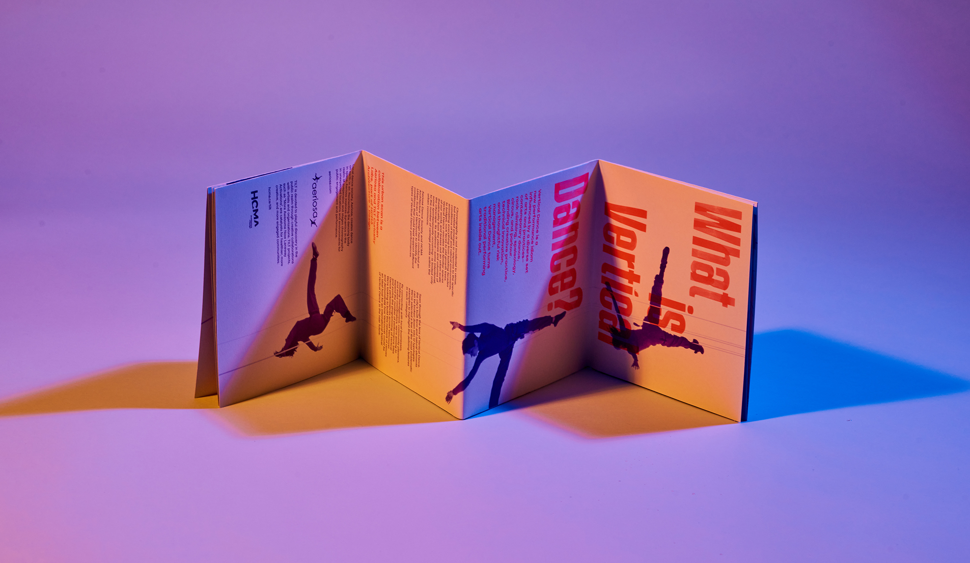 Pink folded pamphlet lying on its side, revealing silhouettes of dancers.