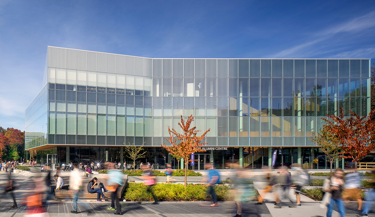 The outside of UBC Robert H. Lee Alumni Centre – a rectangular, glass building with students walking around it.