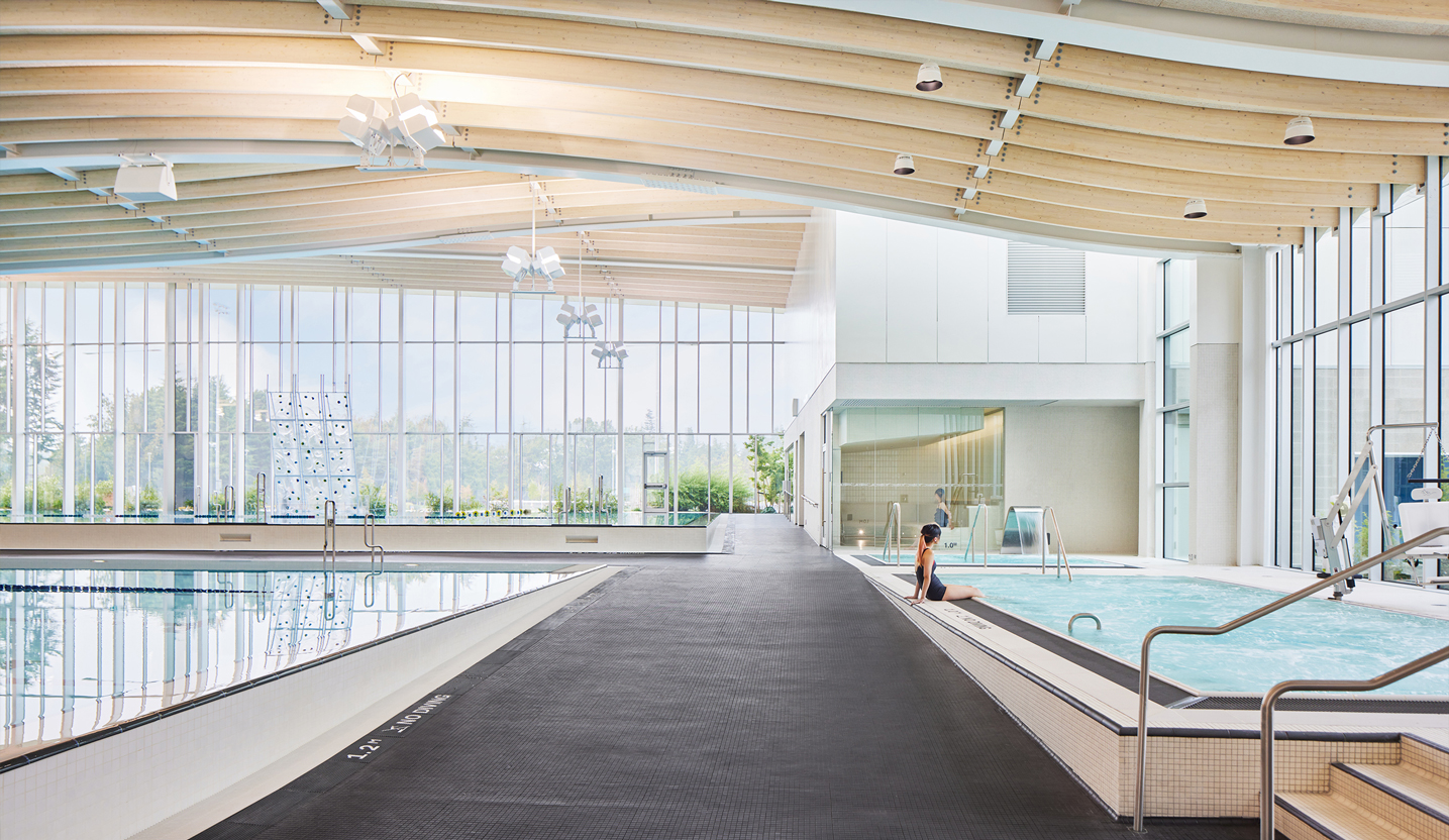 Infinity edge pool, hot tub at Minoru Centre for Active Living. The space features high ceilings, full height windows, and an undulating ceiling.