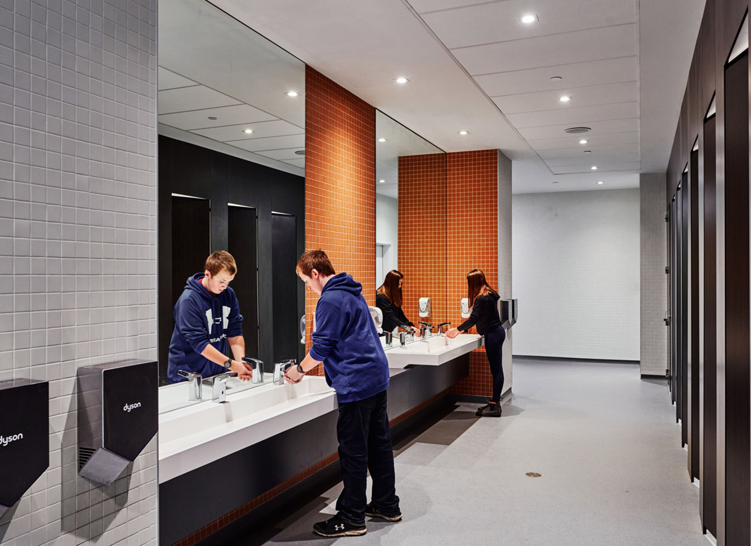 All gender washroom at the high school. A boy and a girl are pictured washing their hands at separate sinks.