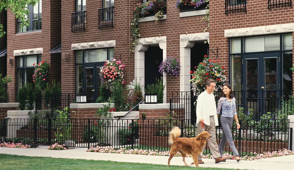 A couple walking their Golden Retriever dog past a brick building.