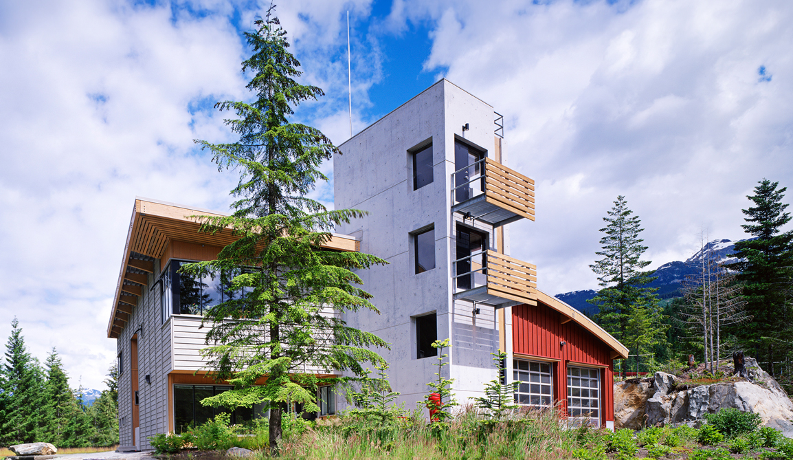 Spring Creek Fire Hall standing amongst the mountains and trees of Whistler, BC, utilizing wooden trims and a large red accent wall.