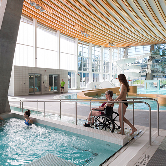 A girl wheeling a woman into the pool in a wheelchair.