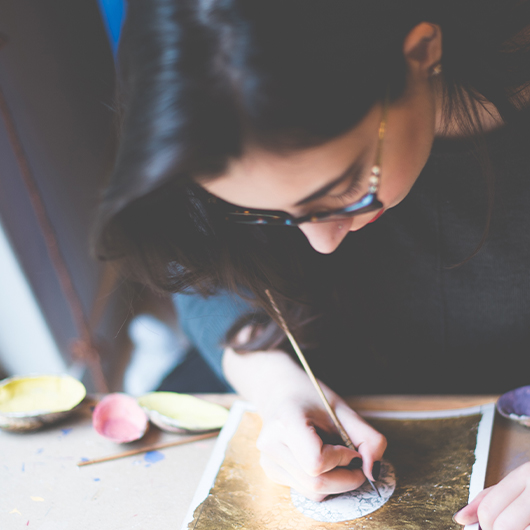 Action shot of Heraa leaning down as she works on one of her paintings.