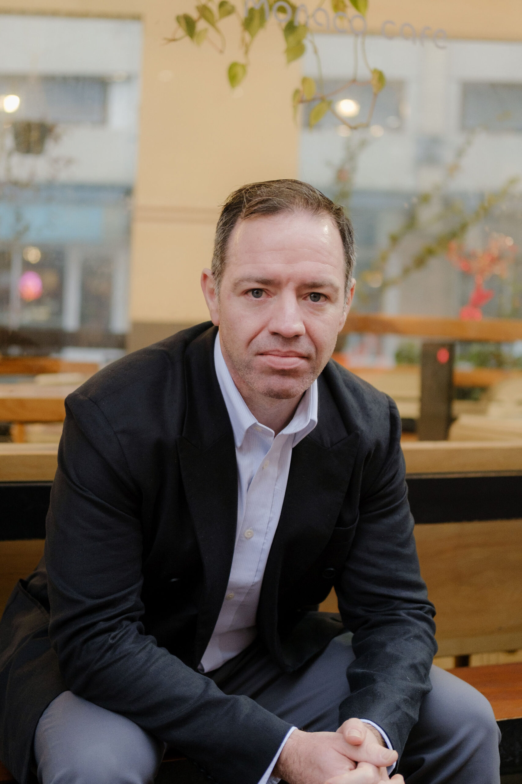 Stuart Farley sits on a bench outside, in front of a cafe window.